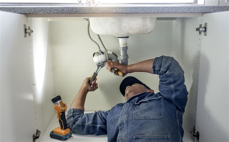 Plumber repairing pipes beneath a bathroom sink in Loma Linda