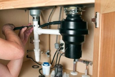 Plumber repairing a garbage disposal beneath a kitchen sink in Loma Linda