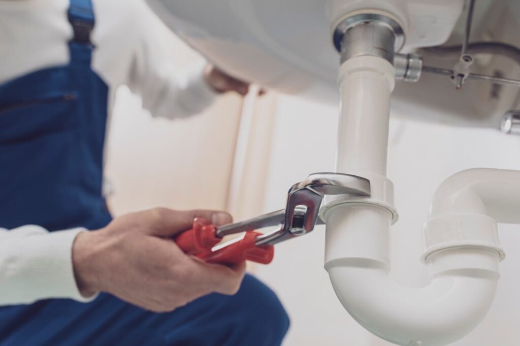 Plumber repairing a white drain pipe beneath a sink in Loma Linda