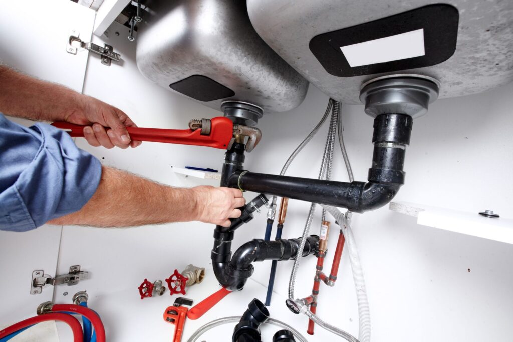 Plumber repairing drain pipes beneath a kitchen sink in Loma Linda
